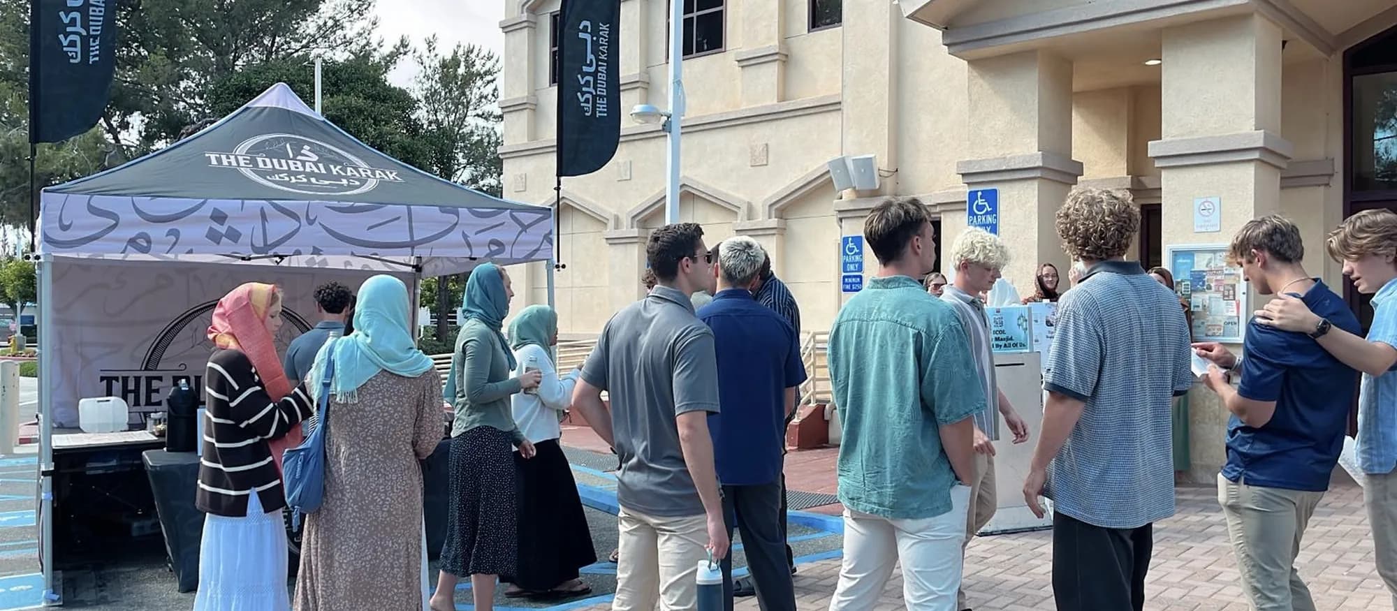 Guests queuing at The Dubai Karak branded canopy booth with feather flags at an outdoor community event in Southern California