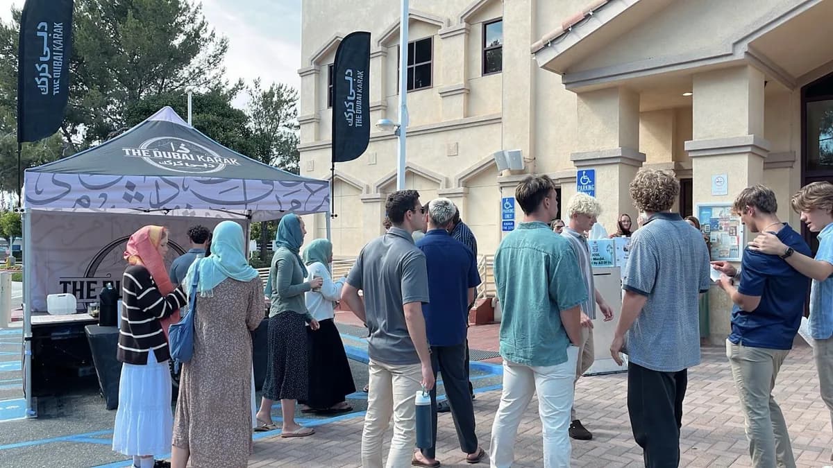 Guests queuing at The Dubai Karak branded canopy booth with feather flags at an outdoor community event in Southern California