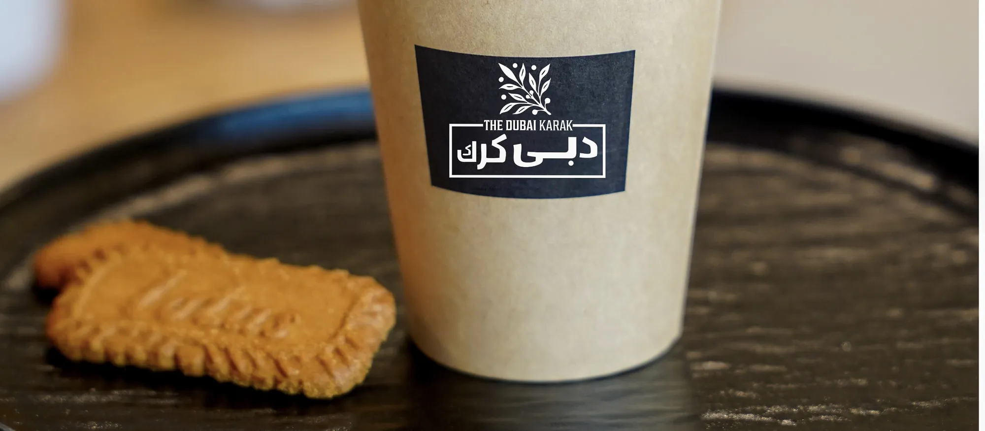 A cup of Dubai karak chai with a caramelised biscuit on a wooden serving board