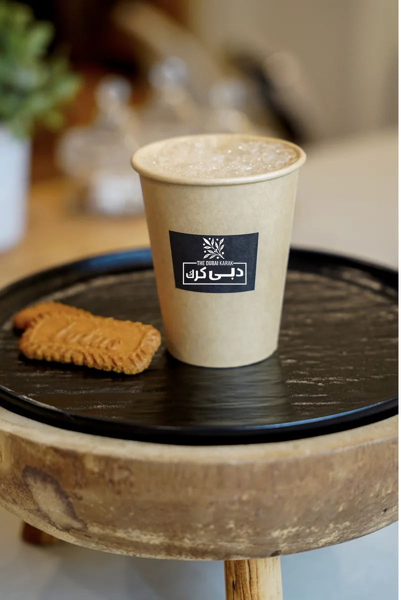 A cup of Dubai karak chai with a caramelised biscuit on a wooden serving board