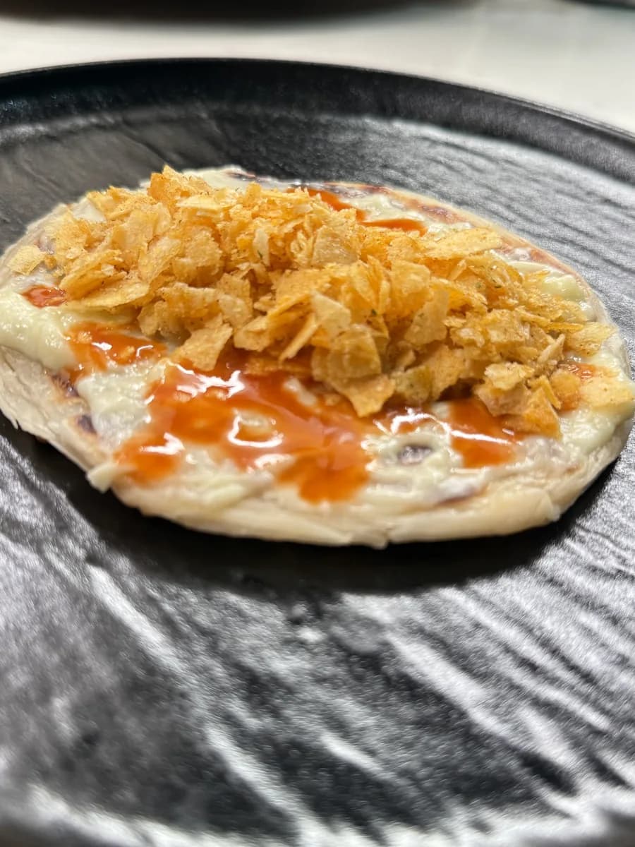 An open Chips Oman and cheese paratha topped with hot sauce on a black plate