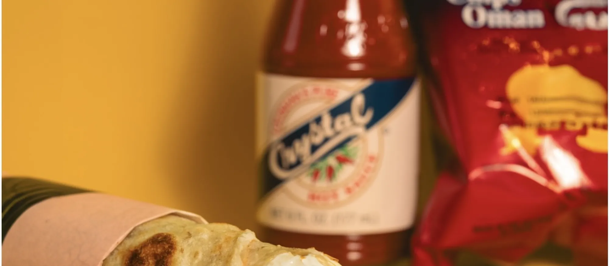 A Chips Oman and cheese paratha wrap with hot sauce and a bag of Chips Oman