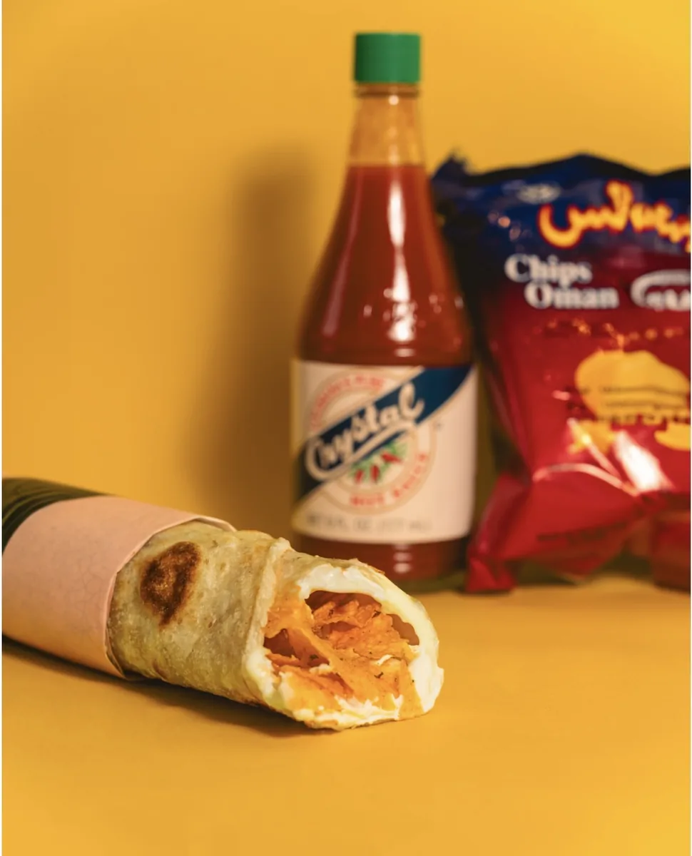 A Chips Oman and cheese paratha wrap with hot sauce and a bag of Chips Oman