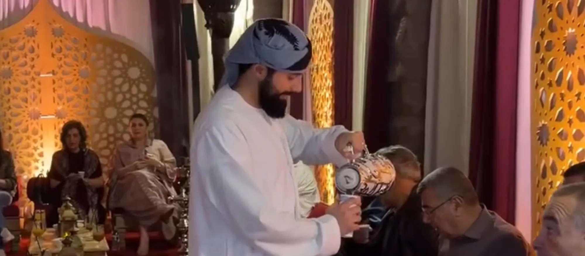 Arabic coffee being poured into small cups for seated guests at a majlis-style cultural event