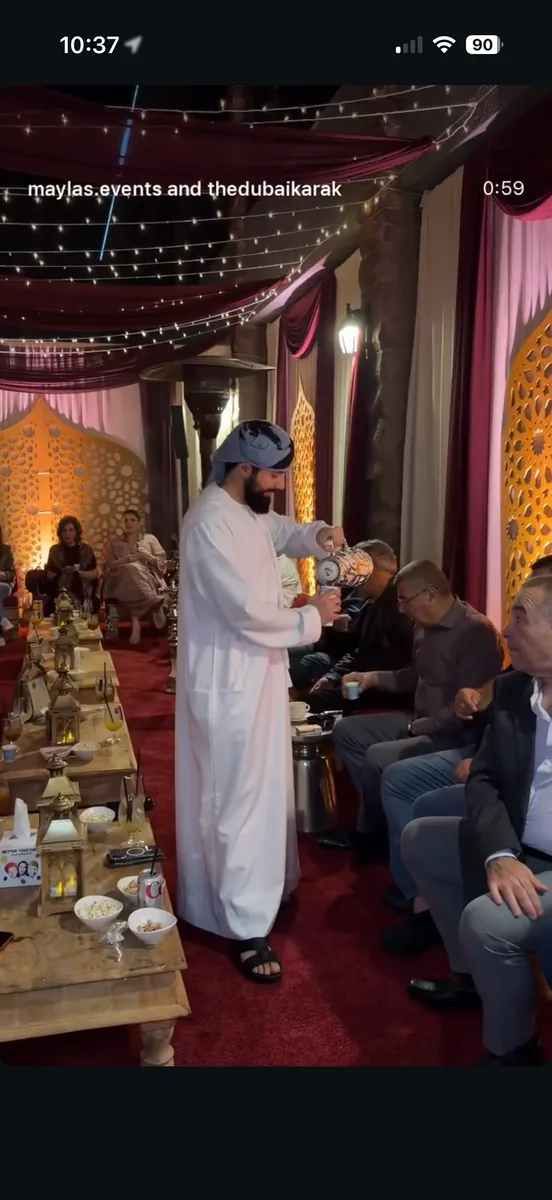 Arabic coffee being poured into small cups for seated guests at a majlis-style cultural event