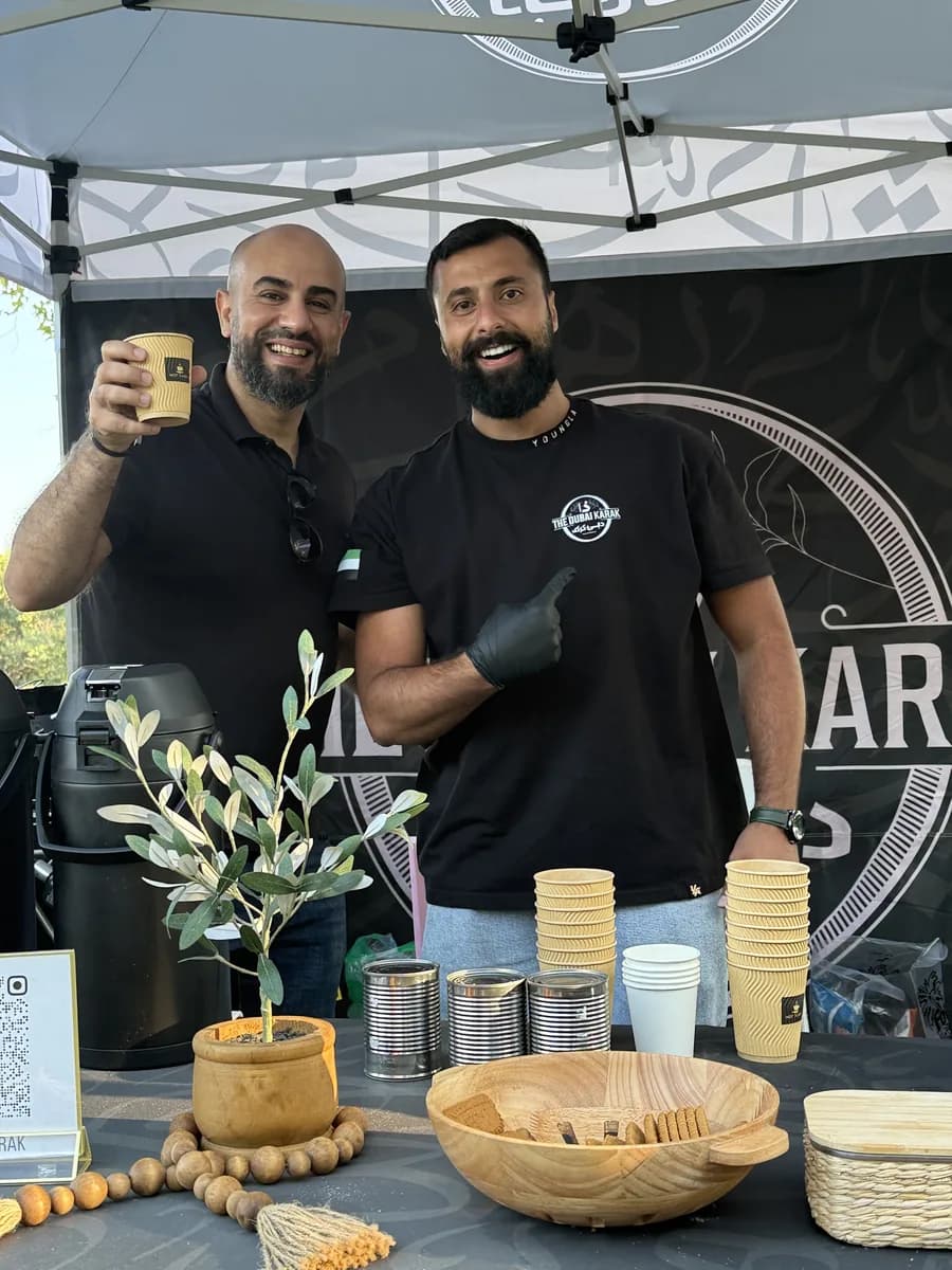 Two members of The Dubai Karak team holding cups of freshly brewed karak chai at their booth