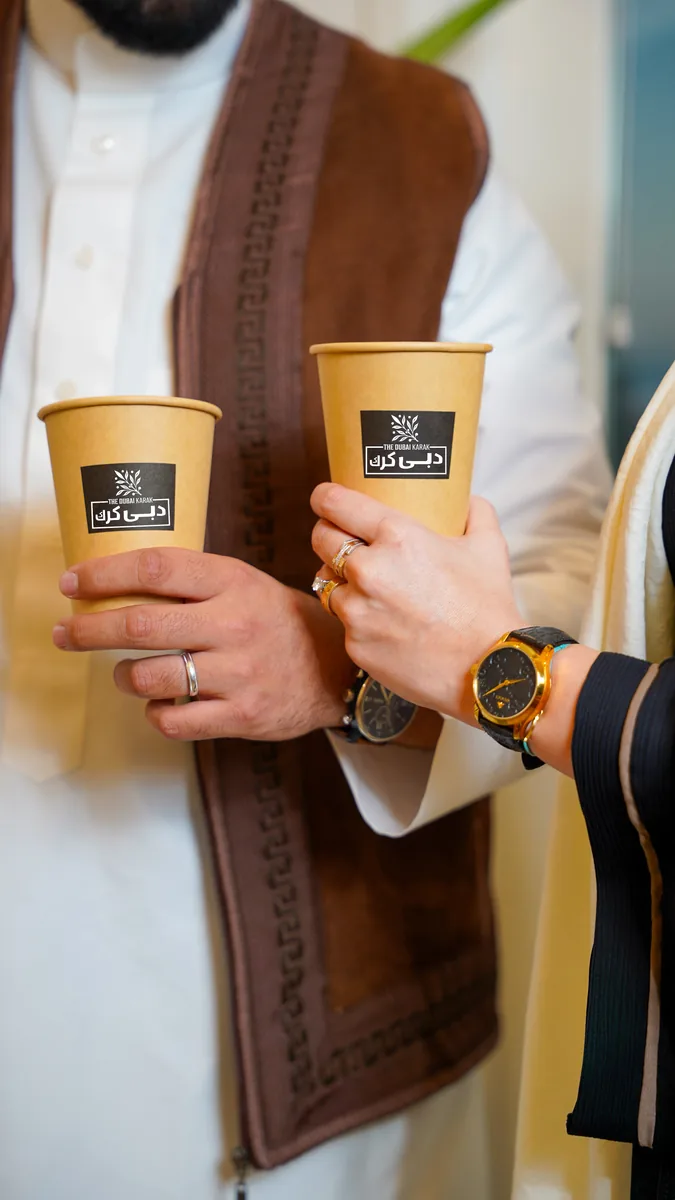 Two guests holding branded cups of Dubai karak chai at an event